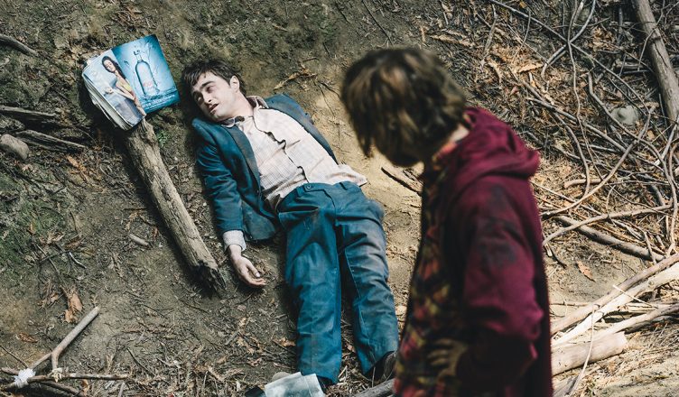 Daniel Radcliffe liegt als Manny am Boden und betrachtet ein Pinup-Magazin während Hank ihn betrachtet