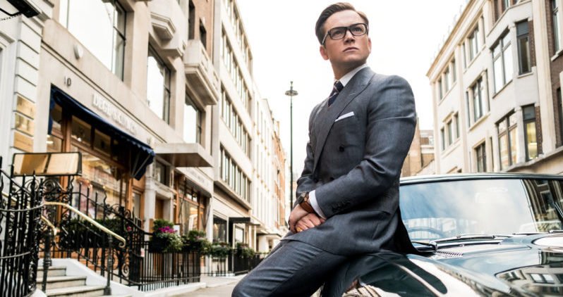 Ein Szenenbild für die Kritik Kingsman The Golden Circle mit Taron Egerton als Eggsy, angelehnt an ein Auto auf einer Straße in London