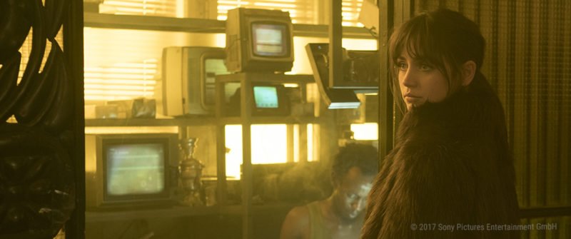 Ana De Armas ist als Replikantin Joi in einem staubigem Raum mit alten TV-Geräten.jpg