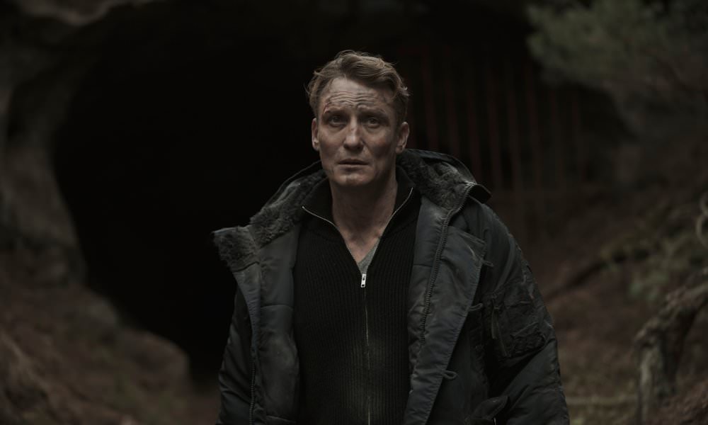 Oliver Masucci als Ullrich vor einer Höhle im Wald in einem Szenenbild der Netflix Serie Dark