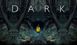 Jonas Kahnwald steht in einer gelben Regenjacke vor einer Höhle in Winden in Dark – Staffel 1