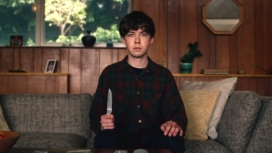 Alex Lawther sitzt auf einem Sofa und hält ein Messer in der Hand im Titelbild für die Kritik The End Of The F***cking World