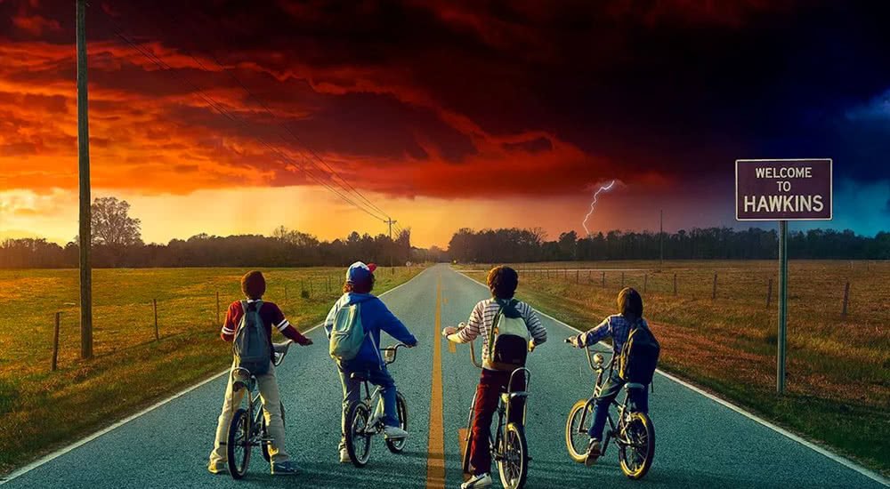 Die vier Hauptfiguren von Stranger Things auf ihren Fahrrad vor einer paranormal roten Wolke über einer Landstraße
