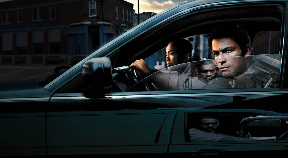 Dominic West als Detective James McNulty beschattet jemanden aus einem schwarzen Auto heraus in The Wire