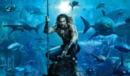 Aquaman (Jason Momoa) sitzt auf einem Felsen unter dem Meer, ausgerüstet mit einem Dreizack.