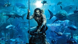Aquaman (Jason Momoa) sitzt auf einem Felsen unter dem Meer, ausgerüstet mit einem Dreizack.