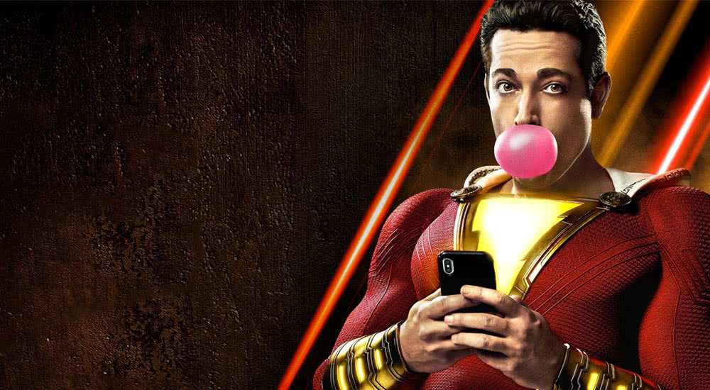 Shazam in Superheldenanzug mit Kaugummi-Blase und Smartphone