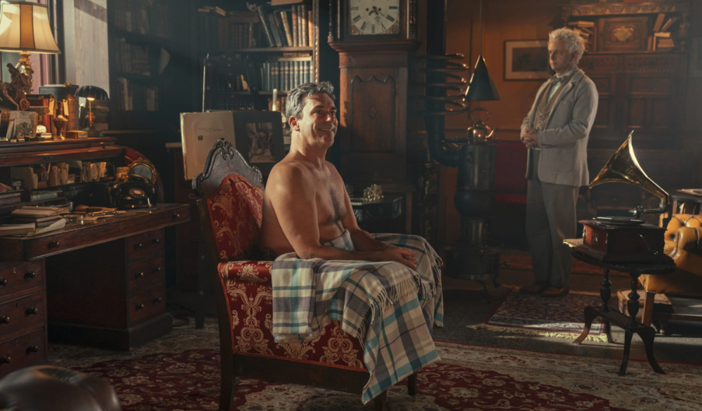 Gabriel (Jon Hamm) nackt auf einem Sessel mit Erziraphael (Michael Sheen) im Hintergrund